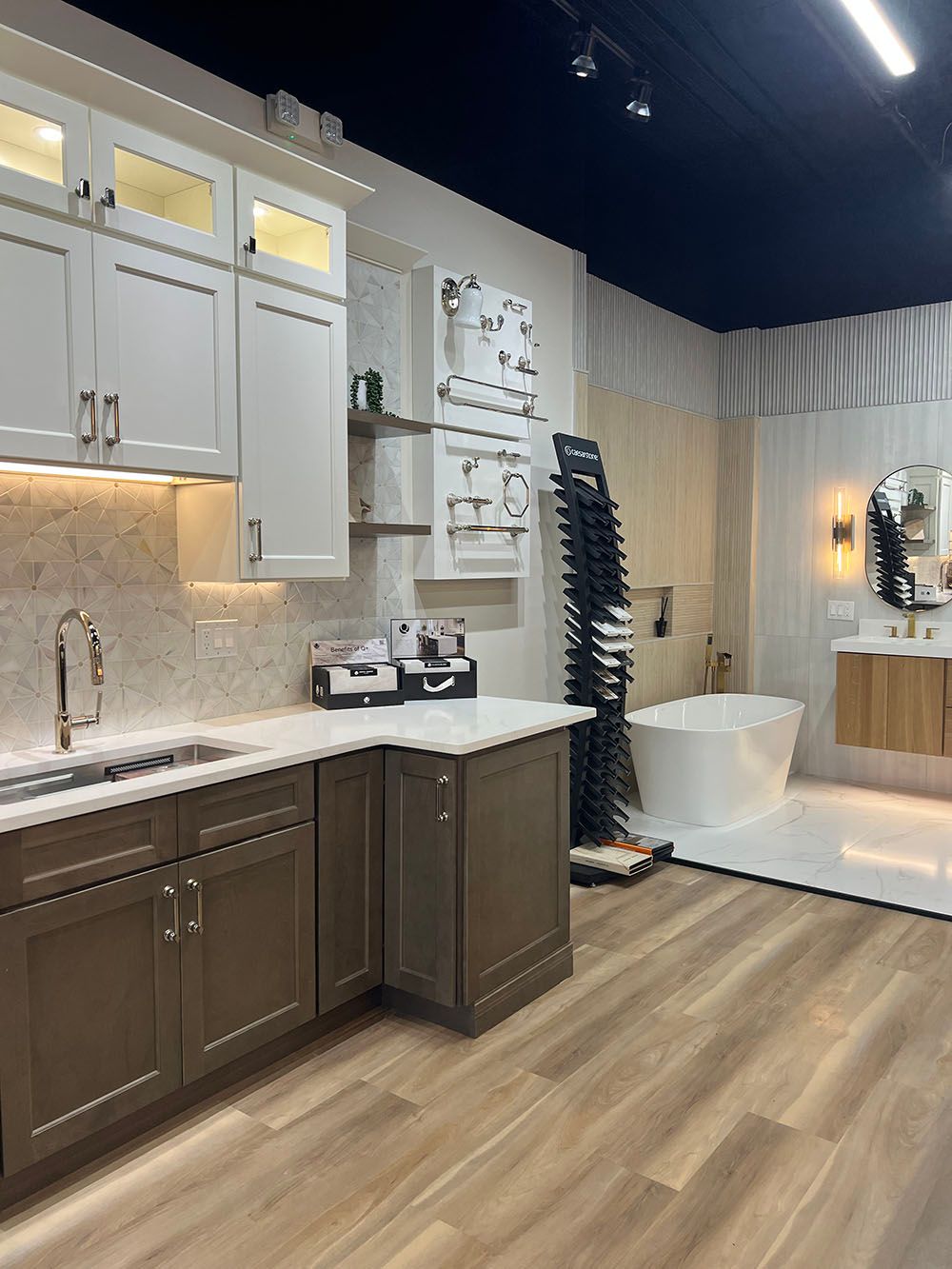 Modern kitchen showroom with gray cabinets, white countertops, wood flooring, and a bathroom display in back.