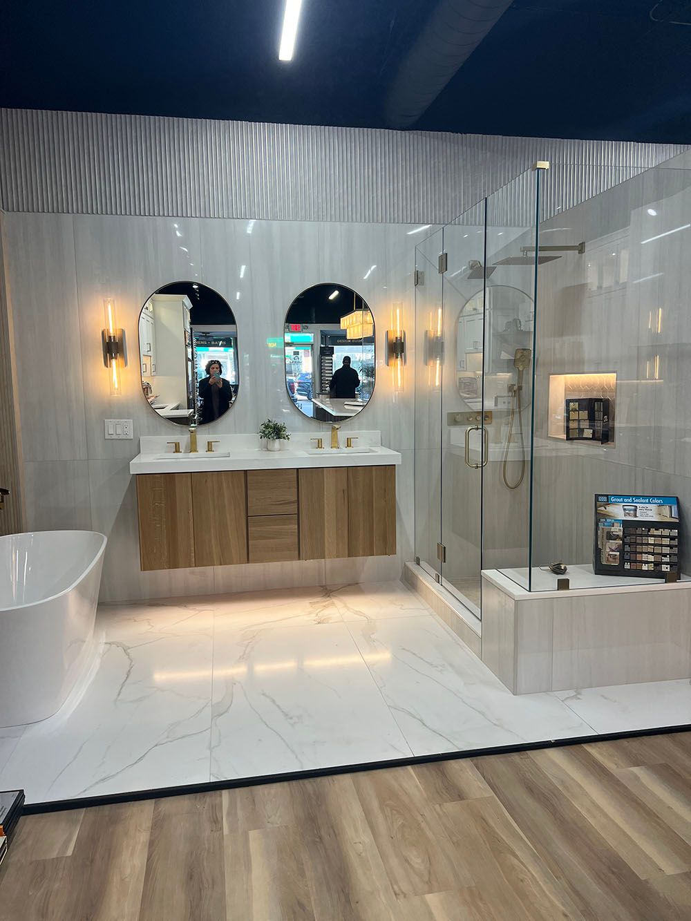 Modern bathroom with double vanity, oval mirrors, glass shower, freestanding tub, and white tile finishes