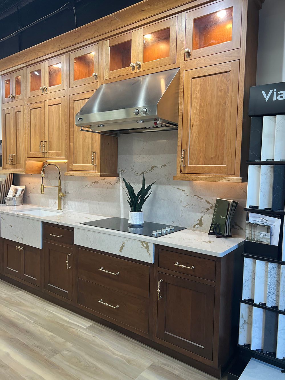 Wooden kitchen cabinetry with marble countertop, farmhouse sink, and stainless range hood under warm lights