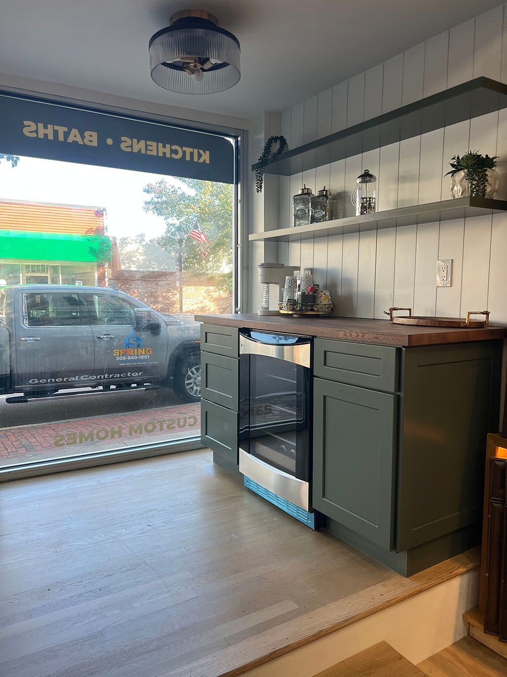 Kitchen interior with green cabinets, black oven, and large front window showing a parked van outside