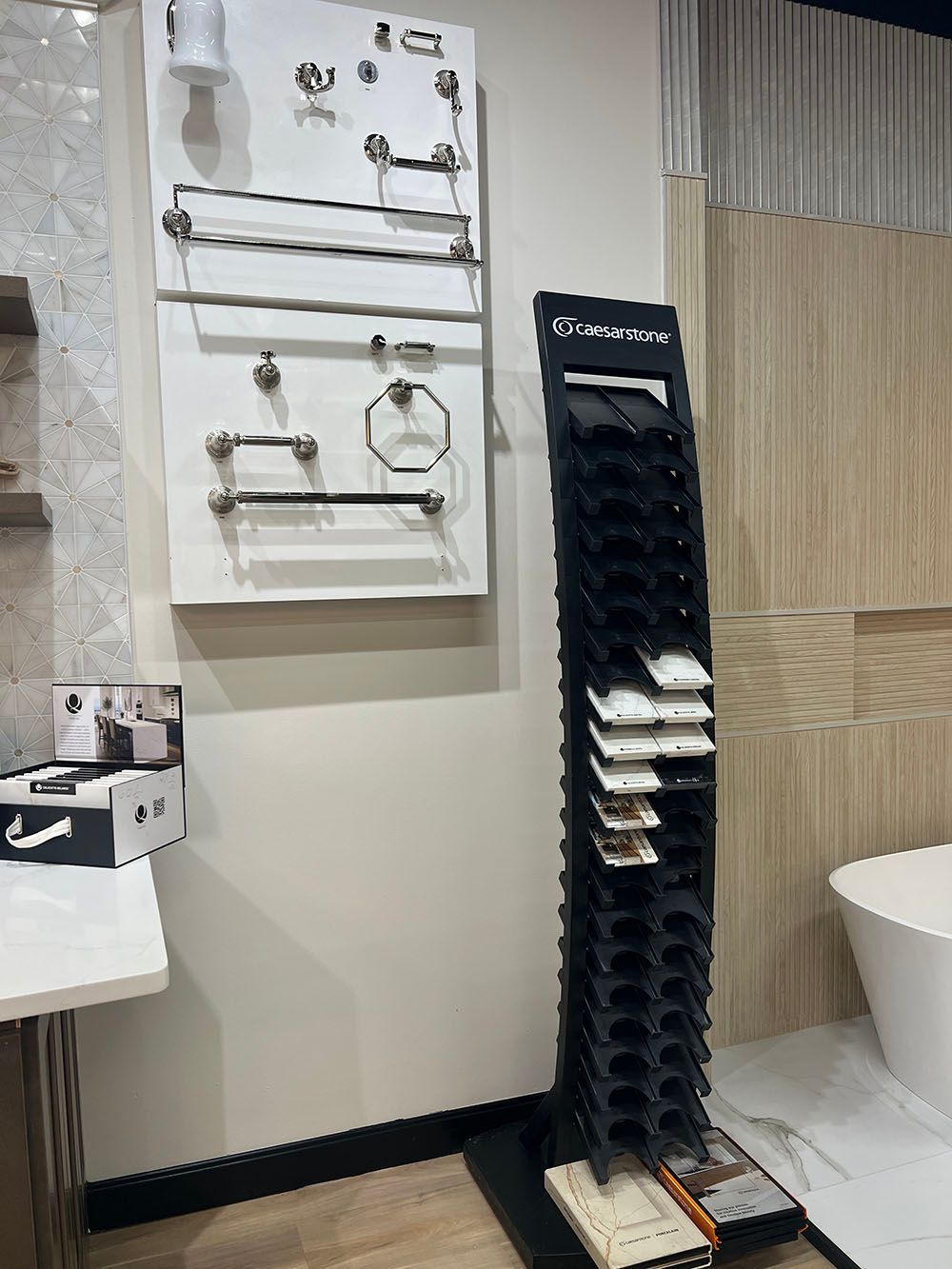Bathroom display with wall-mounted chrome faucets and a tall black towel rack beside a sink and toilet.