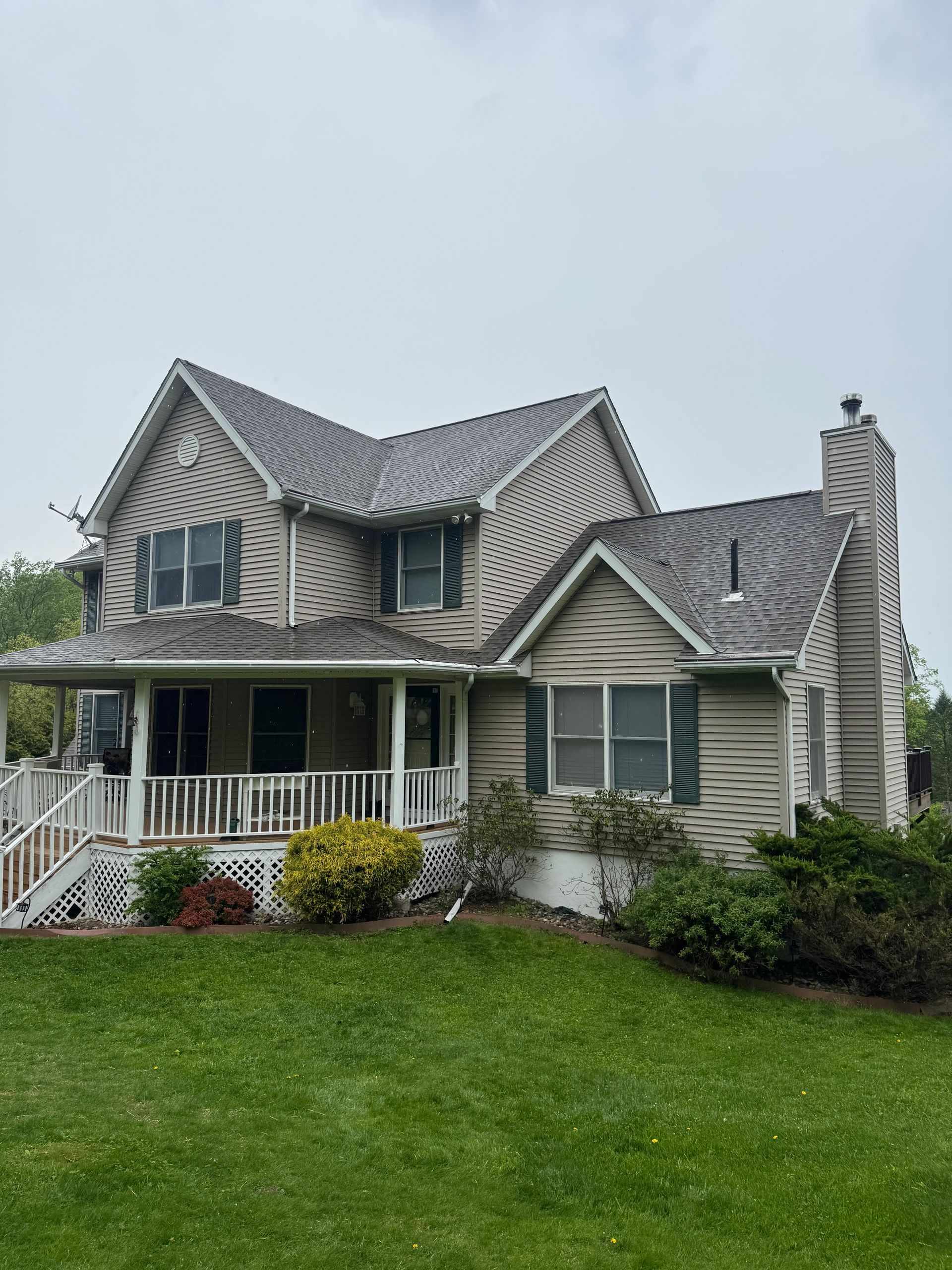 Two-story gray house with a front porch and steep roof, set behind a green lawn