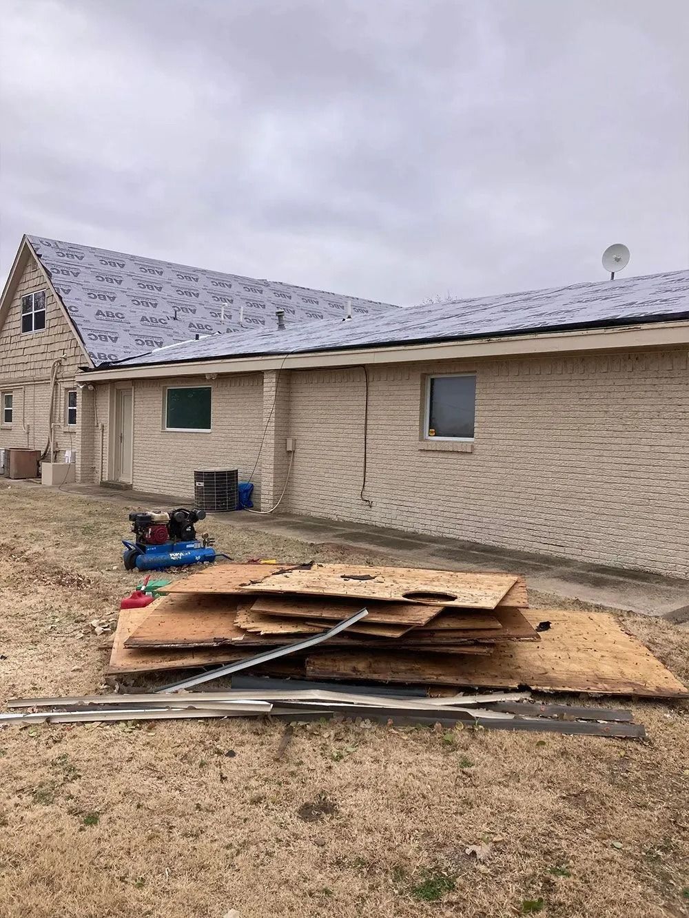 Building exterior with pile of wood scraps in the foreground, cloudy sky.