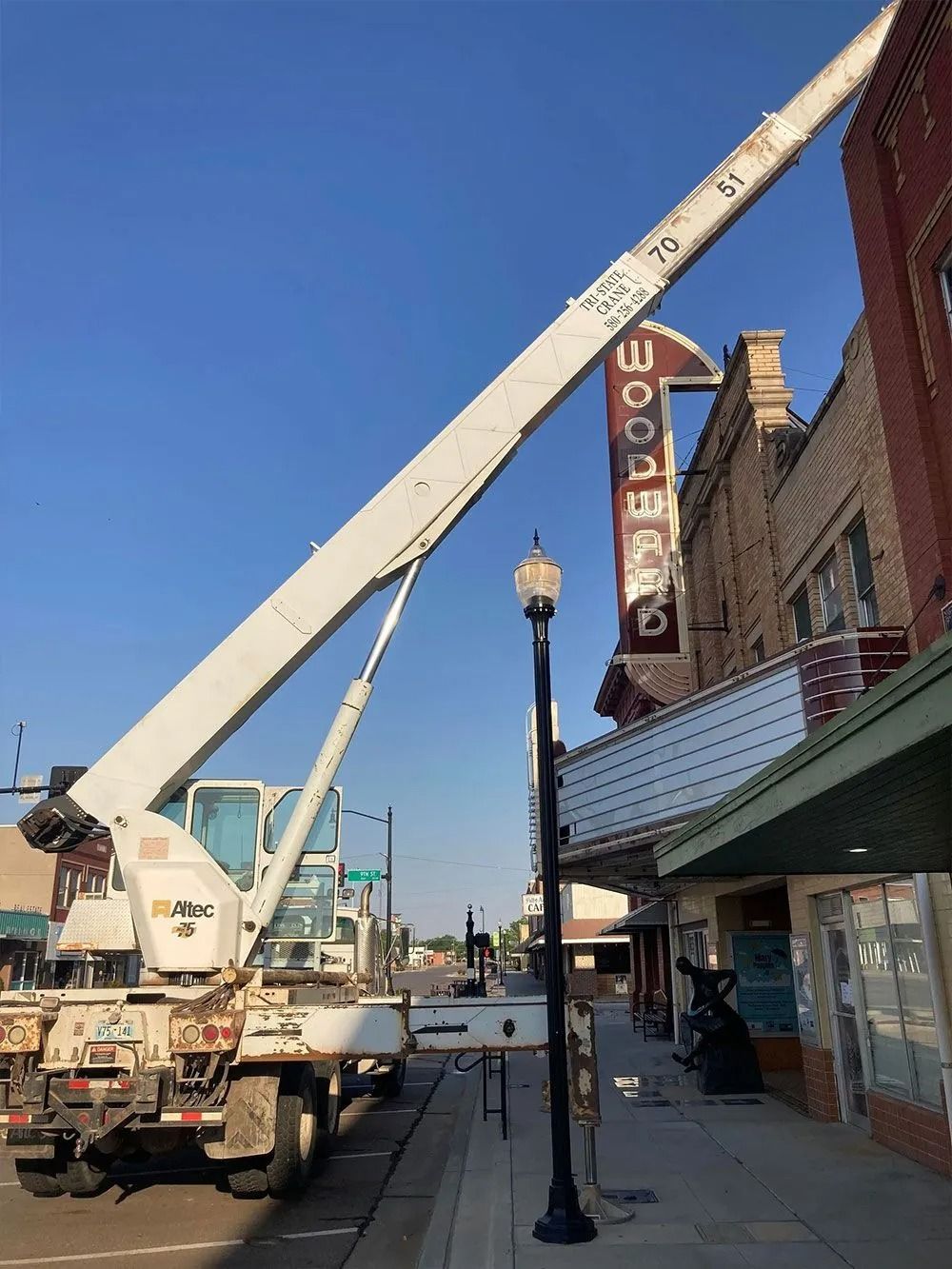 A white crane truck parked on a street next to a brick building with a theater marquee and sign, 