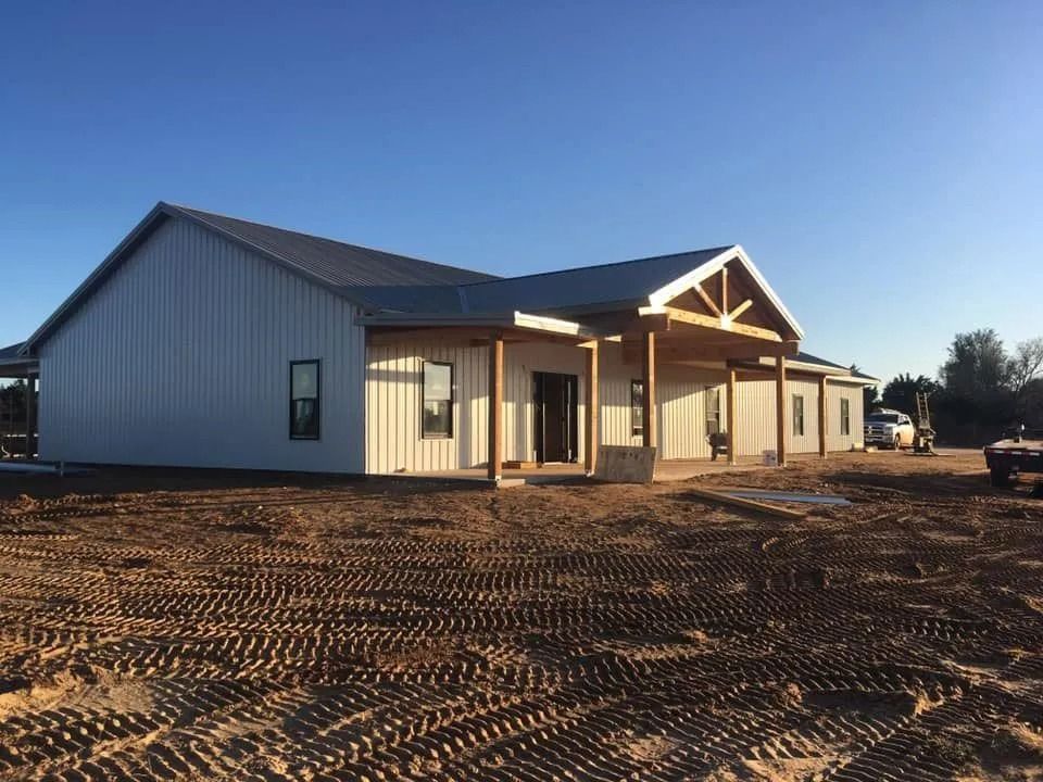 A white metal-sided building under construction with a porch and a clear blue sky.