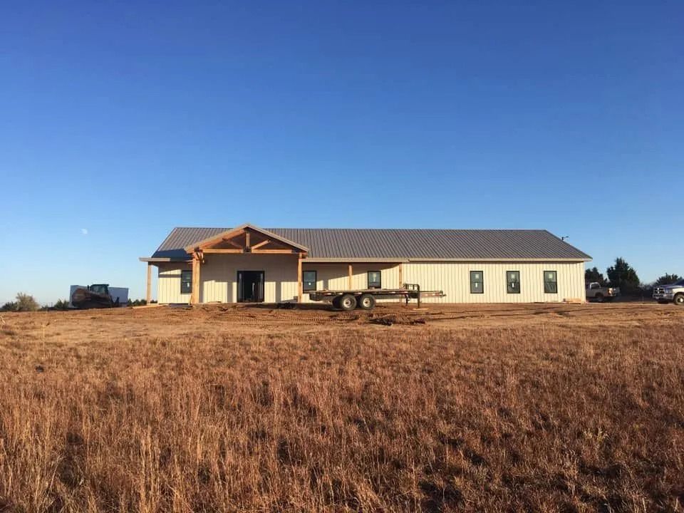 A long, light-colored building under construction in a field, with a blue sky overhead.