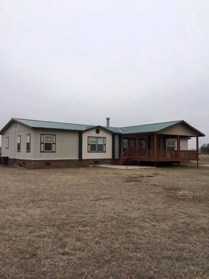Single-story house with green roof, brown deck, and light-colored siding on a cloudy day.