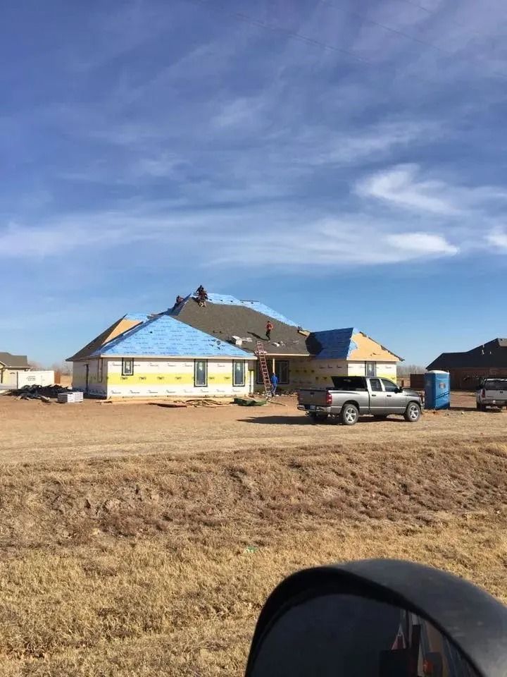House under construction with roofing, blue wrap, and a truck on site.