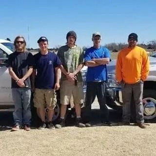 Five men stand in front of a pickup truck on a sunny day.