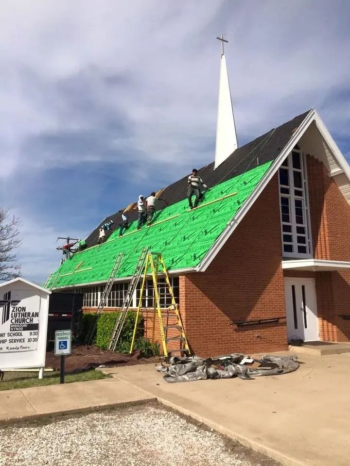 Roofers working on a church roof, installing black shingles over green underlayment; sunny day.