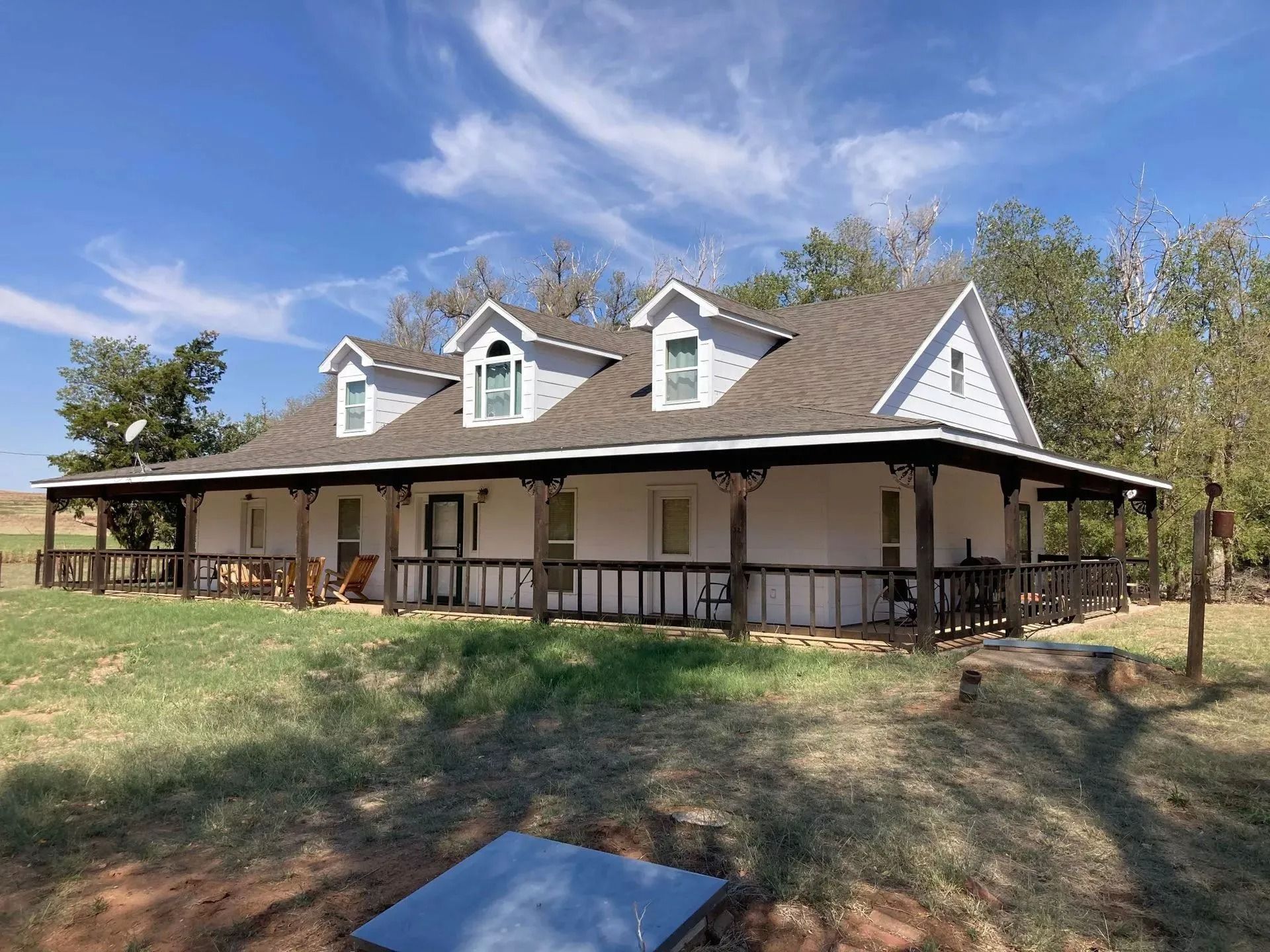 White ranch-style house with dormer windows, surrounded by trees and grass, under a blue sky.