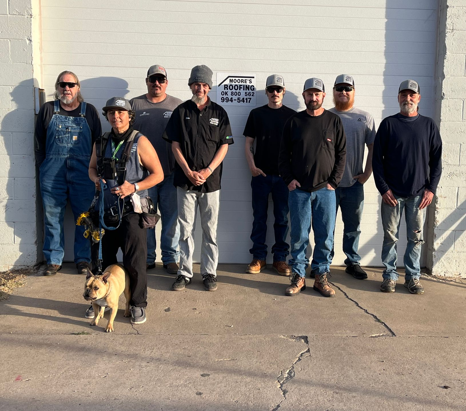 Group of people standing in front of a building. A dog is in front. All are wearing casual clothes.