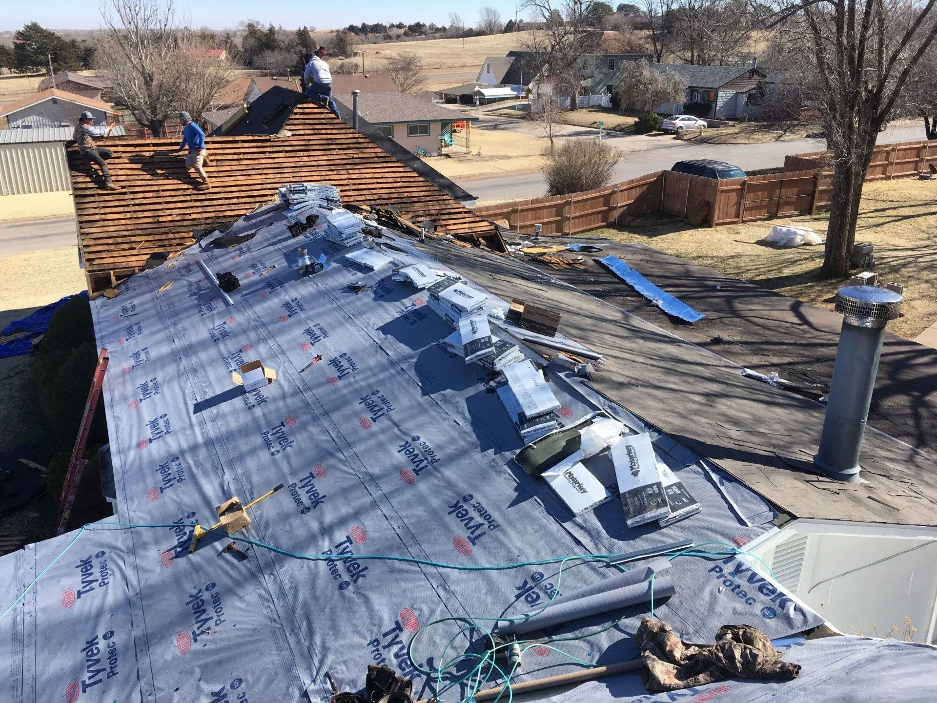 Roofers working on a house roof, removing old shingles and installing new underlayment on a sunny day.