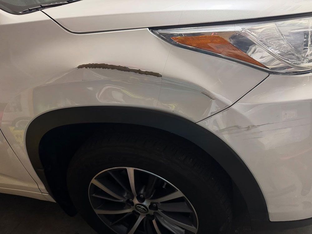 White car with a dented and scratched front fender; rust visible.