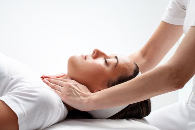 Person receiving a neck massage on a spa table, eyes closed, in a bright white room