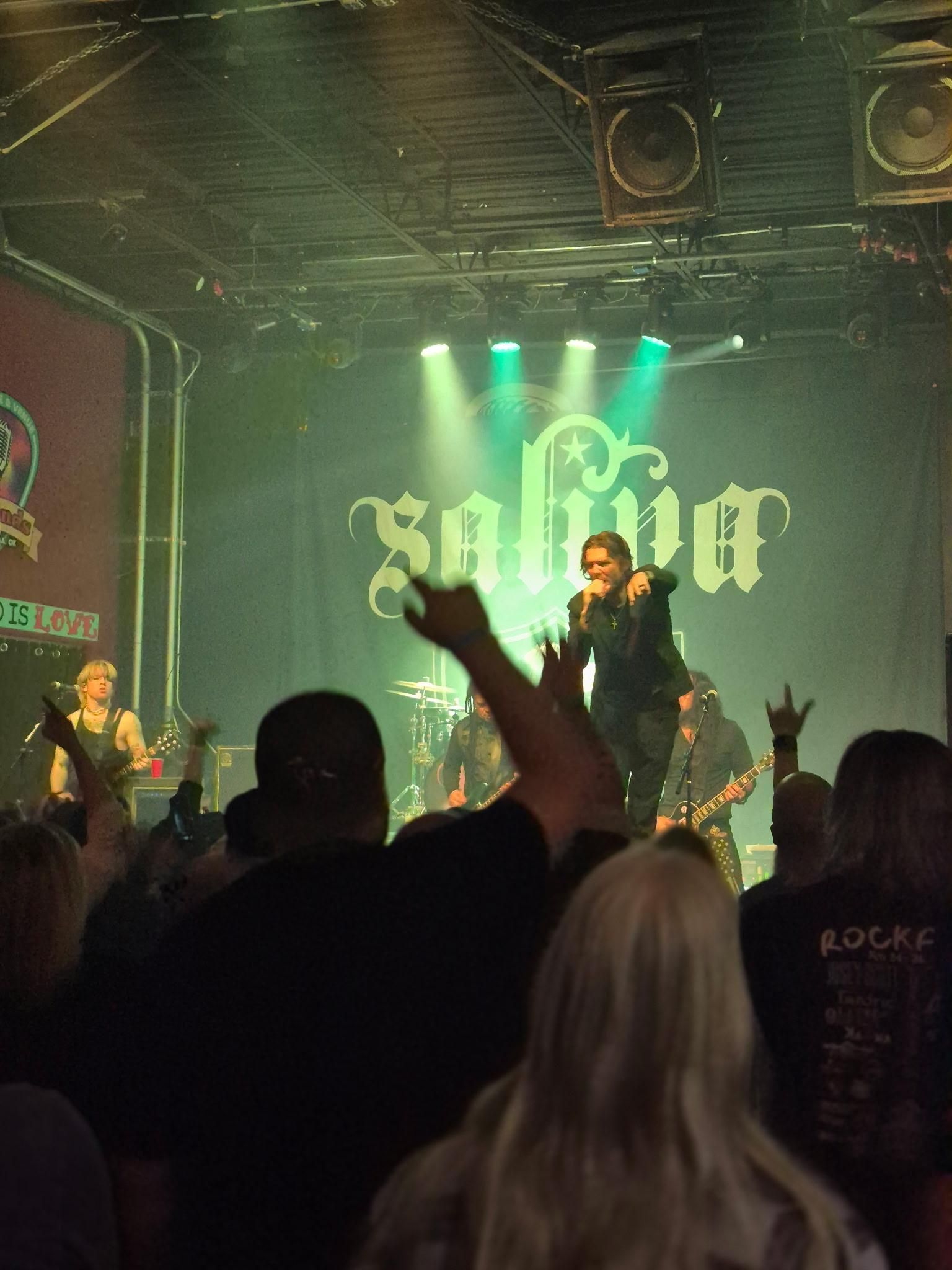 Band Saliva performing on stage in front of a crowd; green stage lights illuminate band logo.