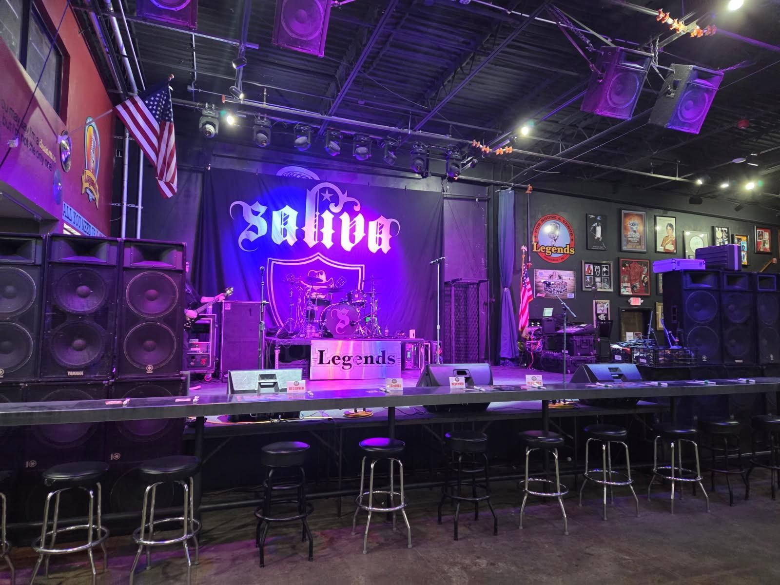 Empty stage with Saliva logo, stage lights, sound equipment, and bar stools.