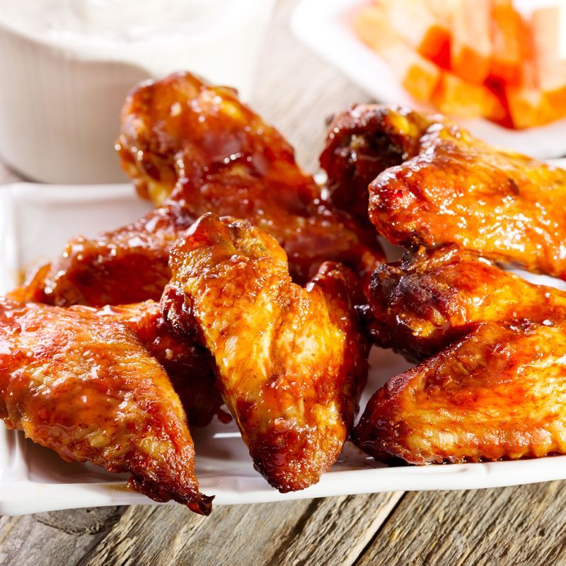 A white plate topped with chicken wings and carrots on a wooden table.