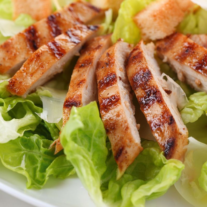 A white plate topped with grilled chicken and lettuce