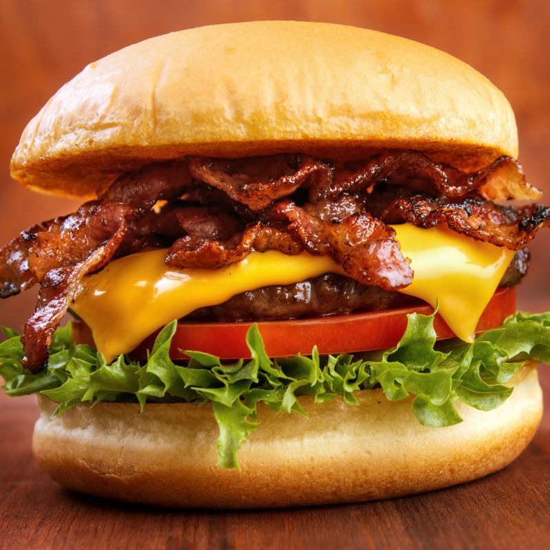A hamburger with cheese, bacon, lettuce and tomato on a bun on a wooden table.