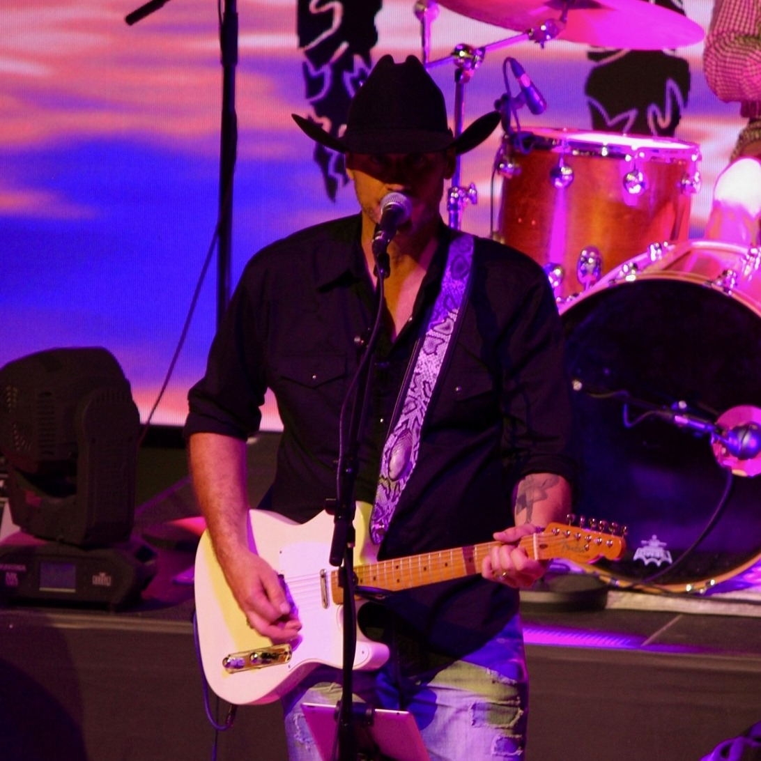 A man in a cowboy hat is playing a guitar and singing into a microphone