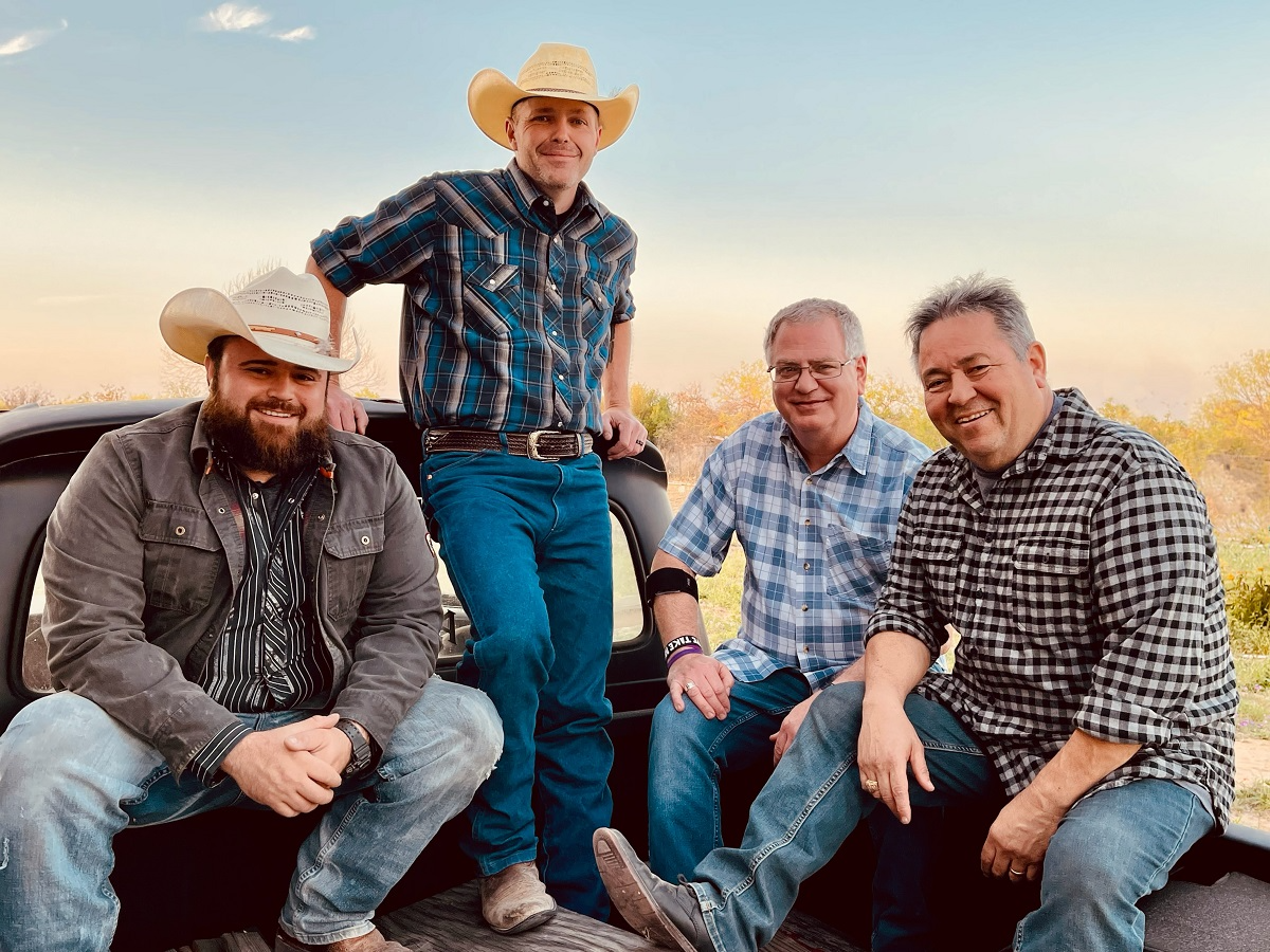 A group of men are sitting on the back of a truck.