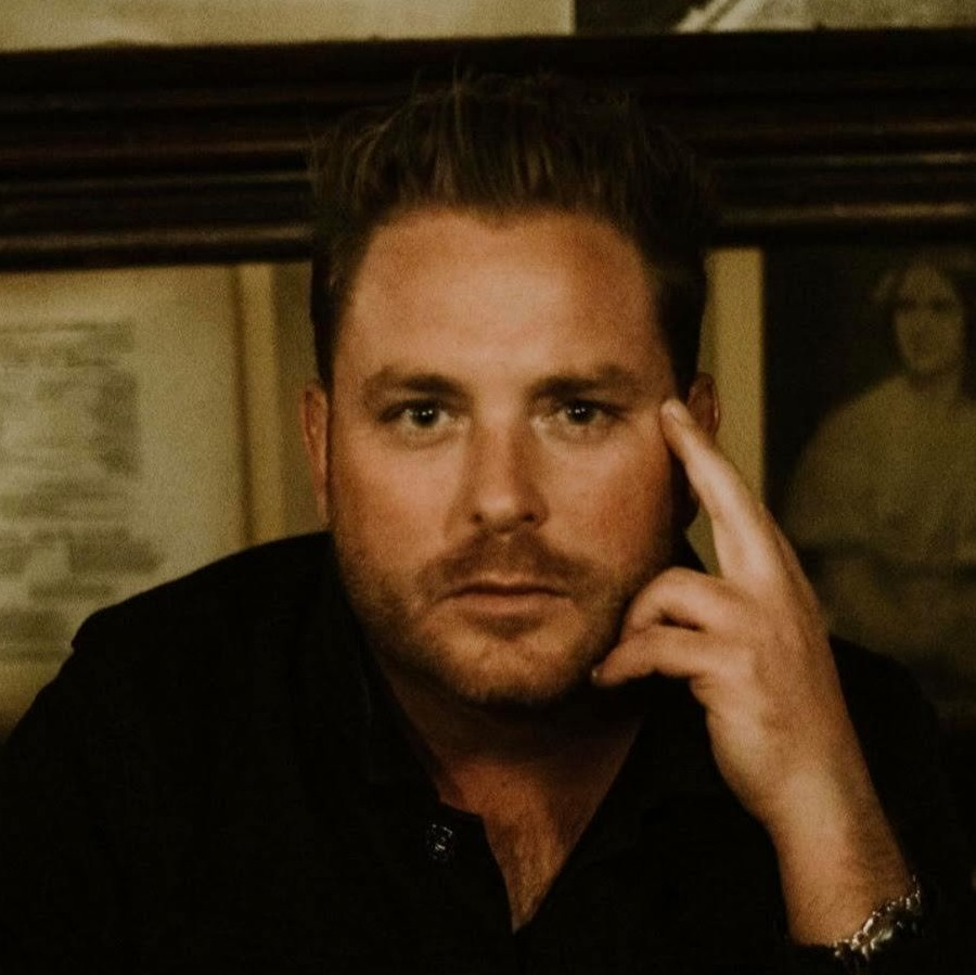 A man in a black shirt holds his finger to his forehead