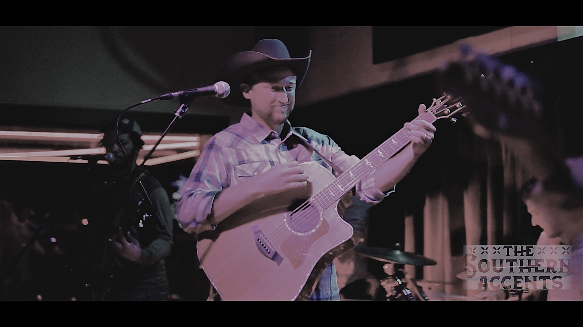 A man in a cowboy hat is playing a guitar on stage