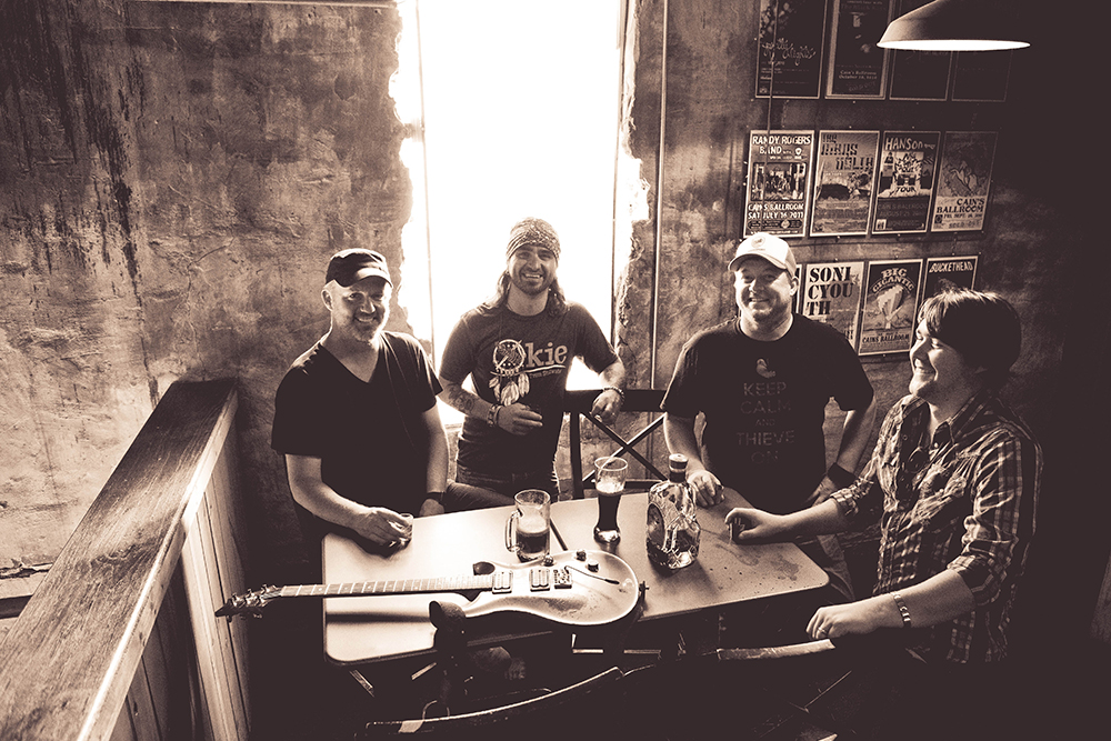 A group of men are sitting around a table with a guitar.