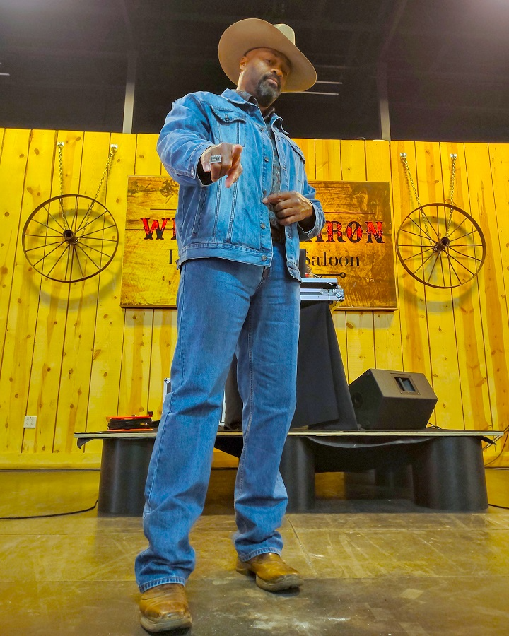 A man in a cowboy hat stands in front of a sign that says warrior