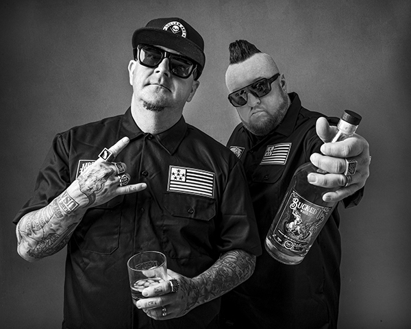 Two men are standing next to each other holding bottles of alcohol.