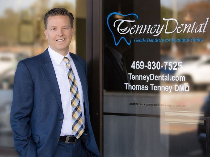 A man in a suit and tie is standing in front of a dental office