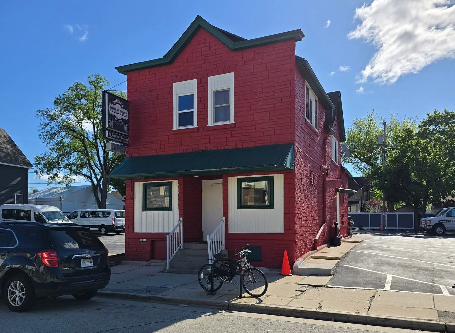 A bright red, two-story brick building with white trim, a green awning, and a bicycle parked out front on a sunny day.