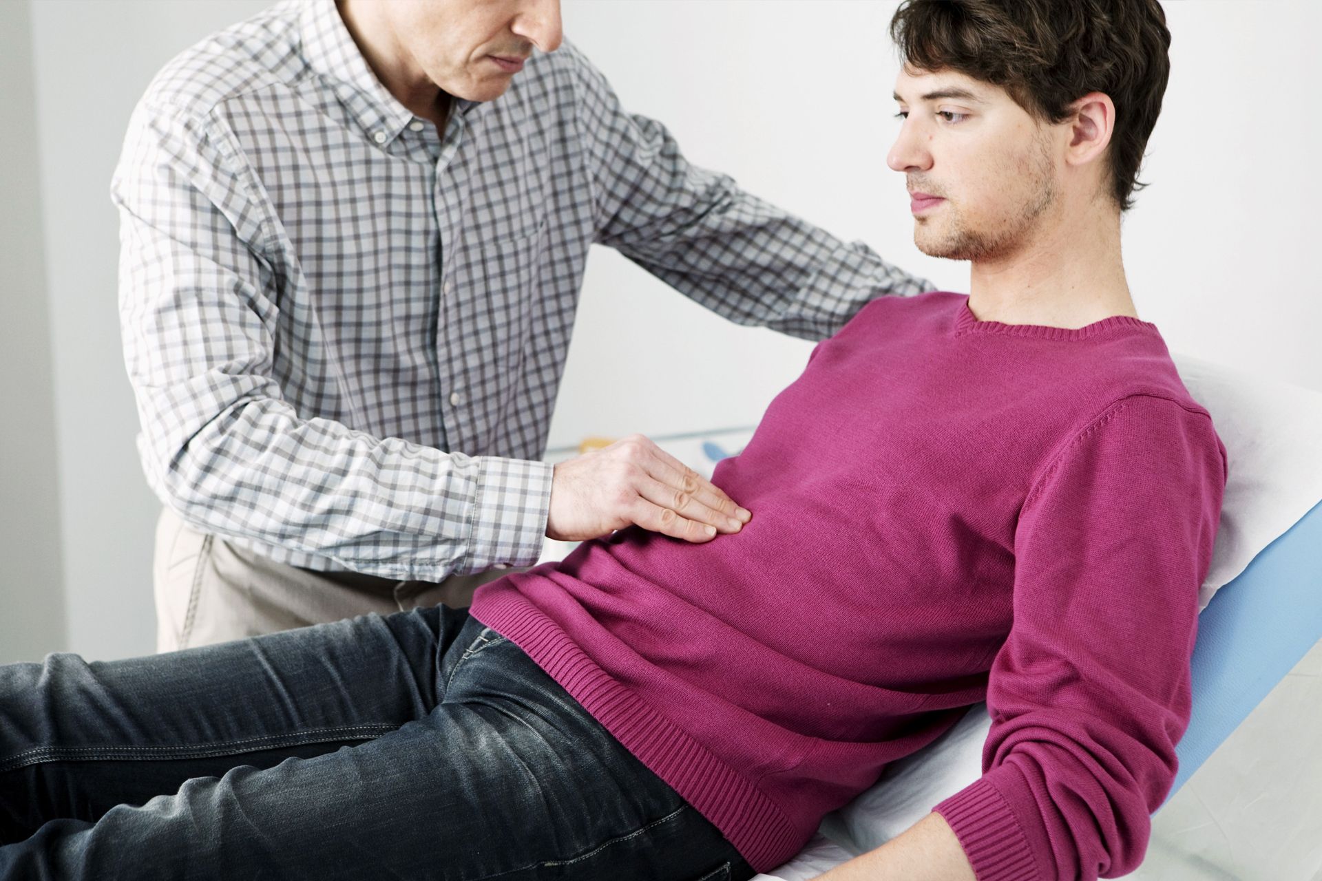 Doctor examining a patient's abdomen in a medical setting.