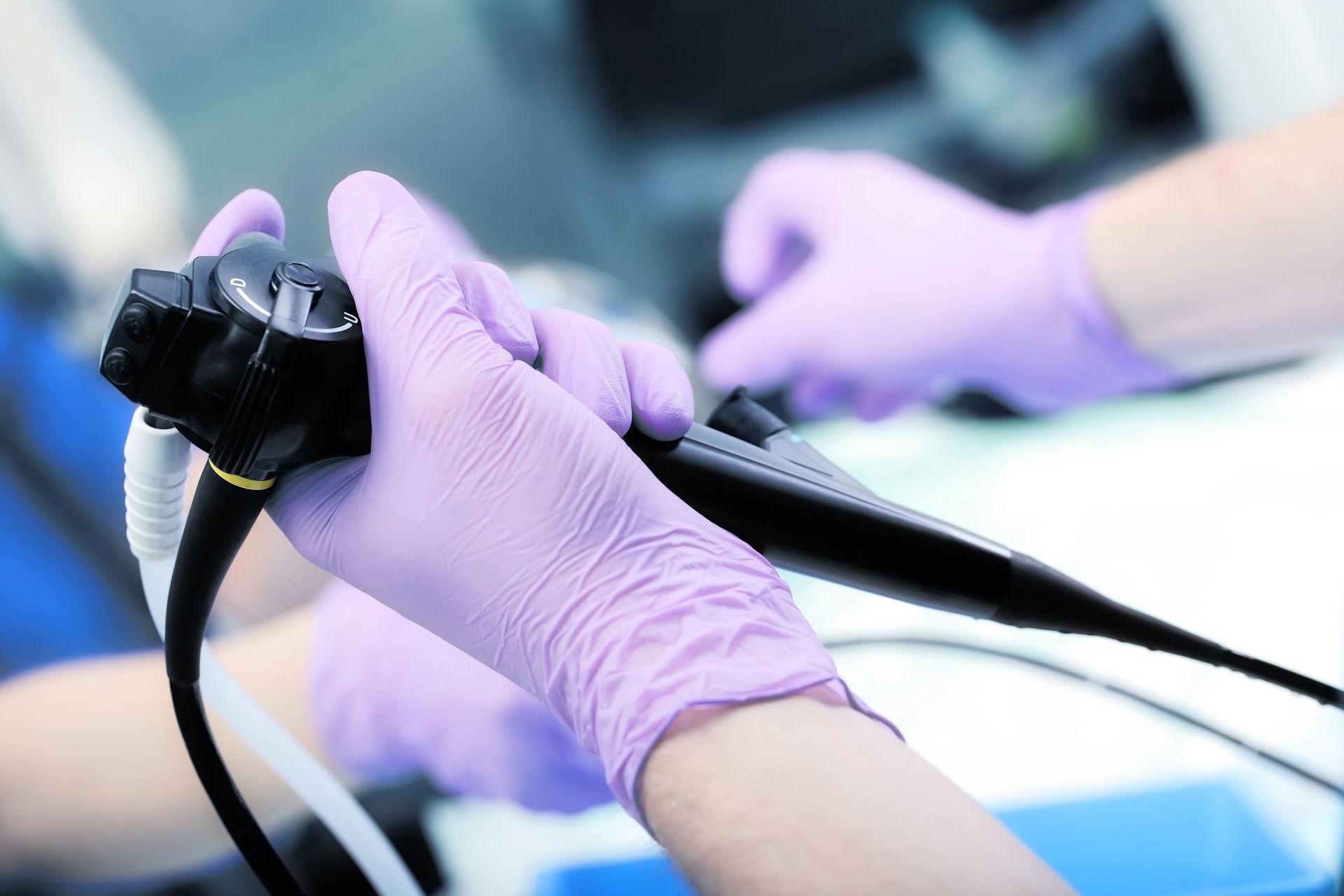 Hands in purple gloves holding an endoscope, medical setting.