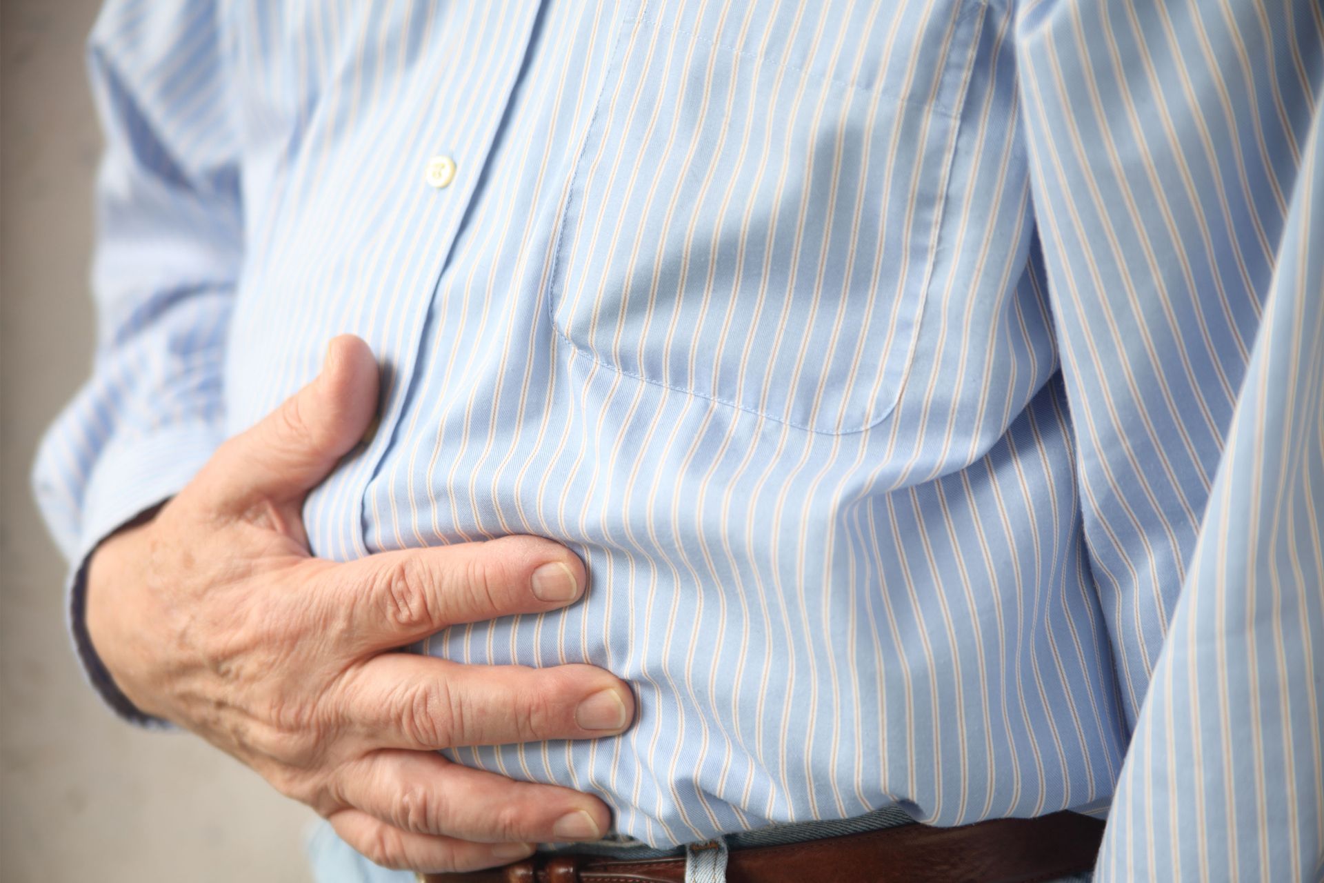 Man holding his abdomen, wearing a light blue striped shirt.