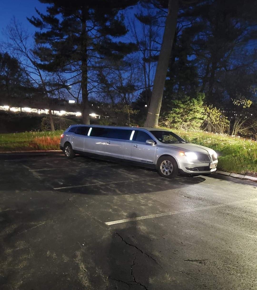 A silver limousine is parked in a parking lot at night
