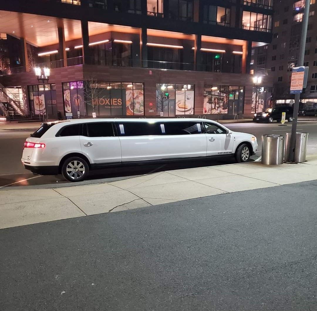 A white limousine is parked on the side of the road in front of a building.
