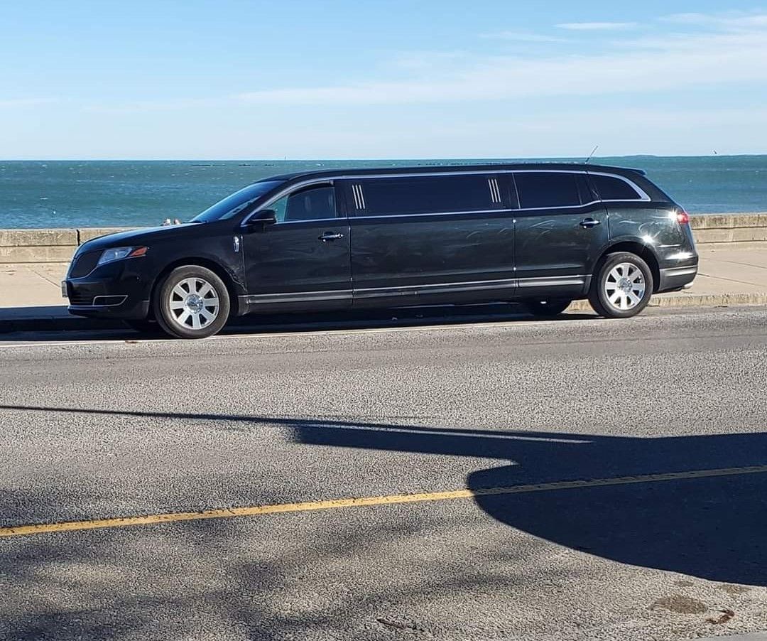 A black limousine is parked on the side of the road near the ocean.