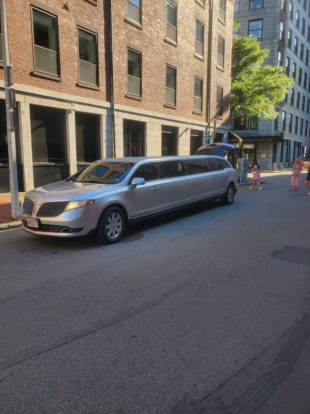 A silver limousine is parked on the side of the road in front of a brick building.