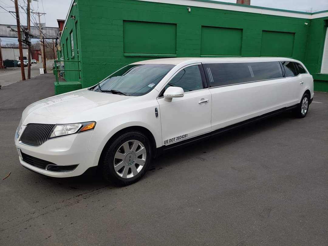 A white limousine is parked in front of a green building.