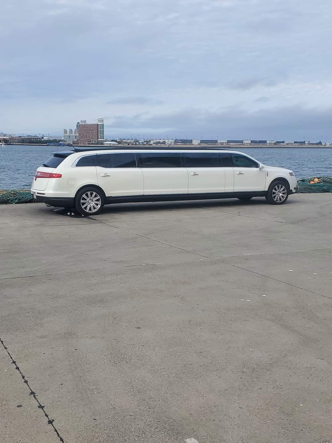 A white limousine is parked in a parking lot next to a body of water.