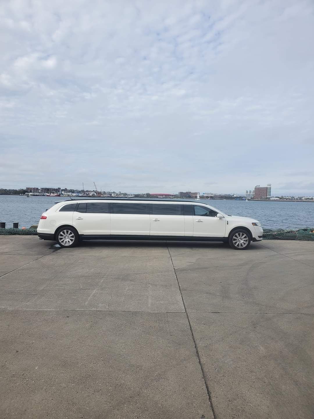 A white limousine is parked in a parking lot next to a body of water.