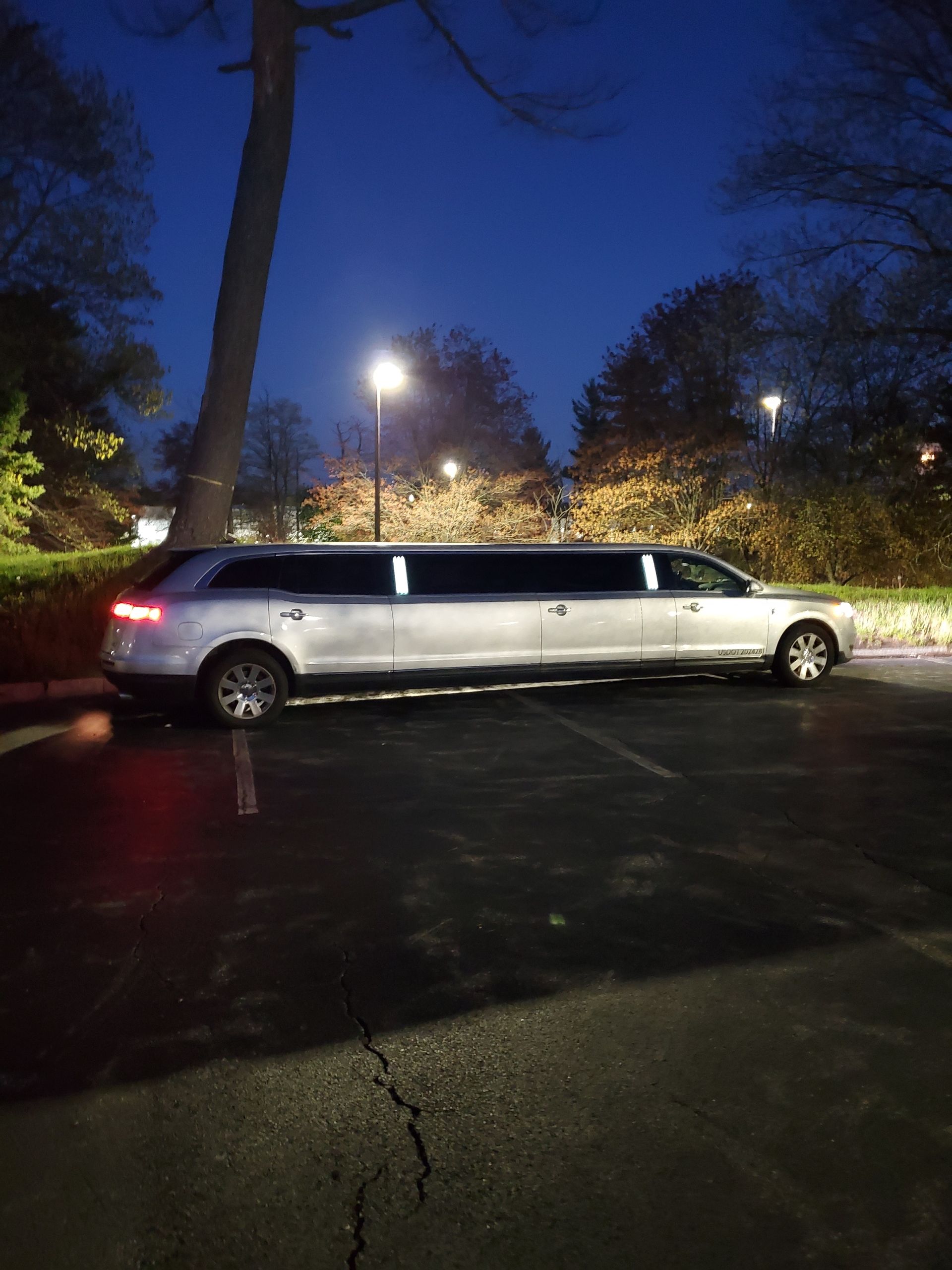 A white limousine is parked in a parking lot at night