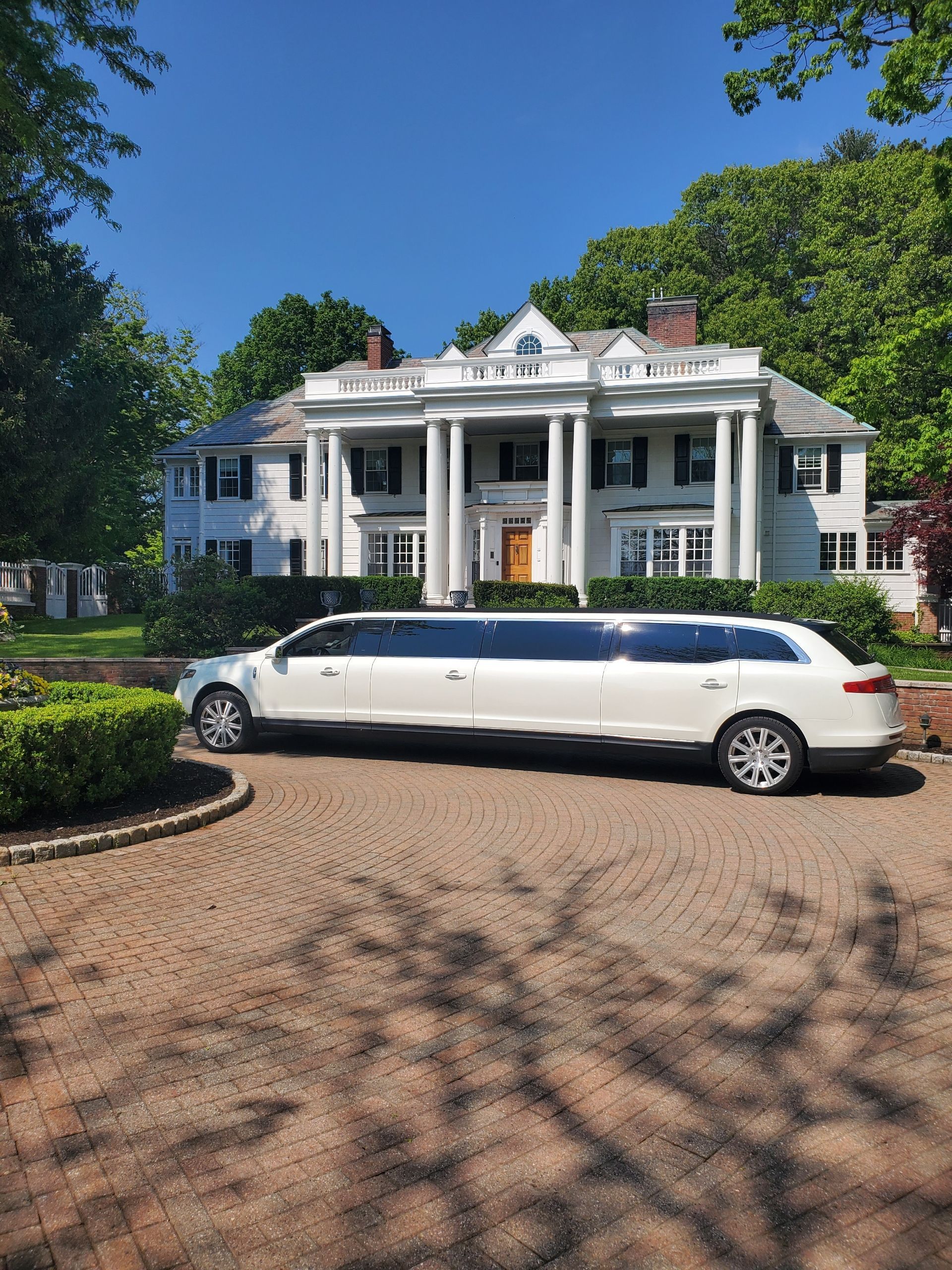 A white limousine is parked in front of a large white house.