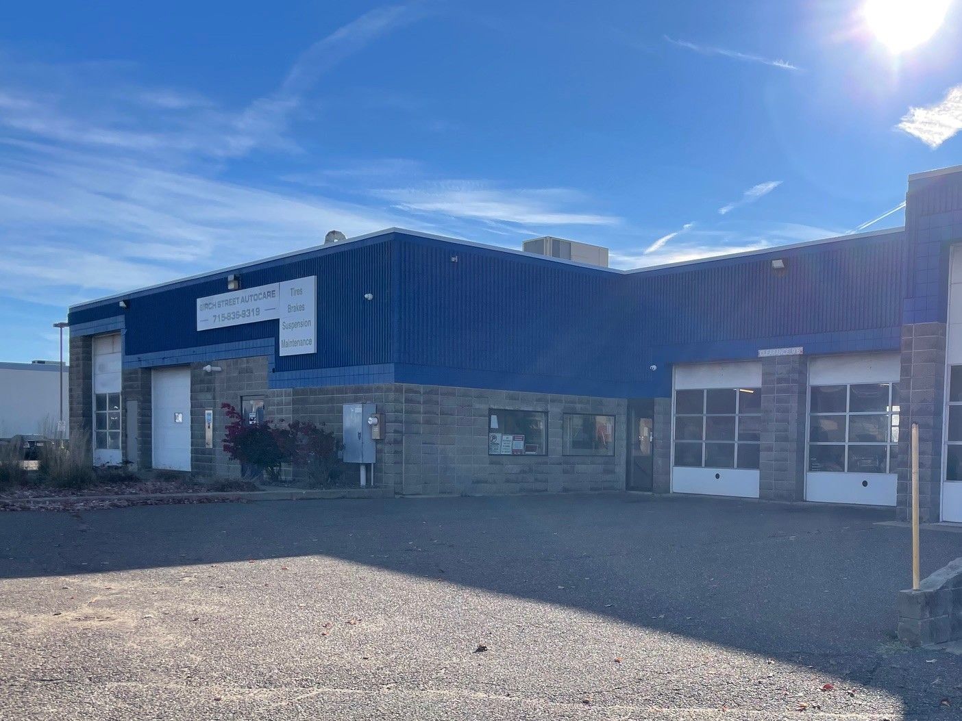 Blue industrial warehouse with gravel lot and bright sunlight.