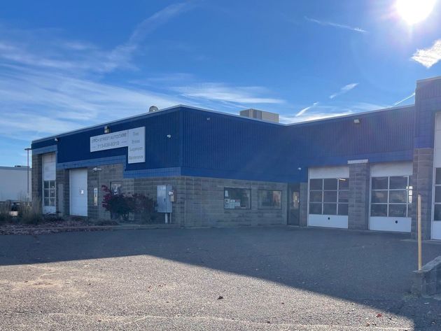 Blue industrial warehouse with gravel lot and bright sunlight.