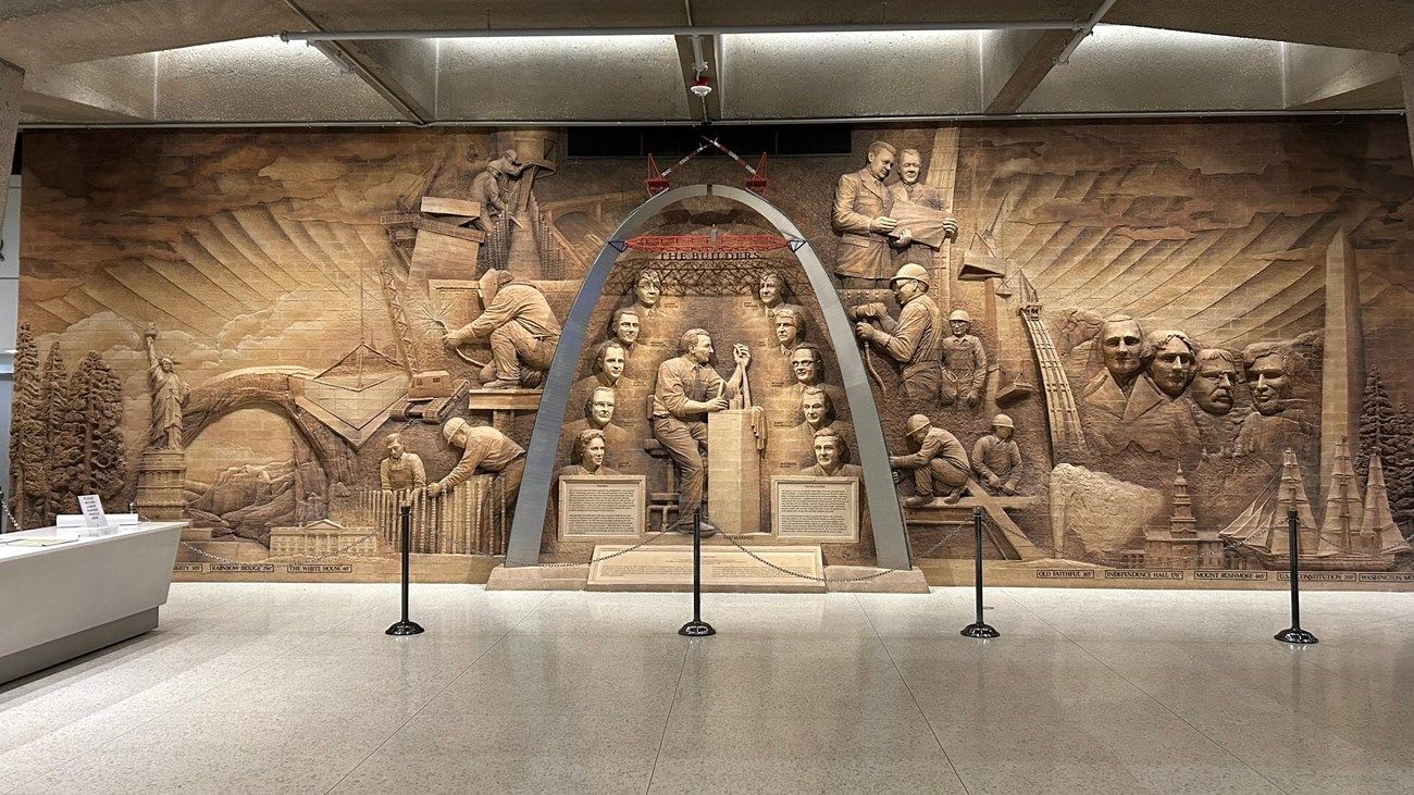 Museum wall relief of an ancient carved stone scene with arches and figures, lit by gallery lights.