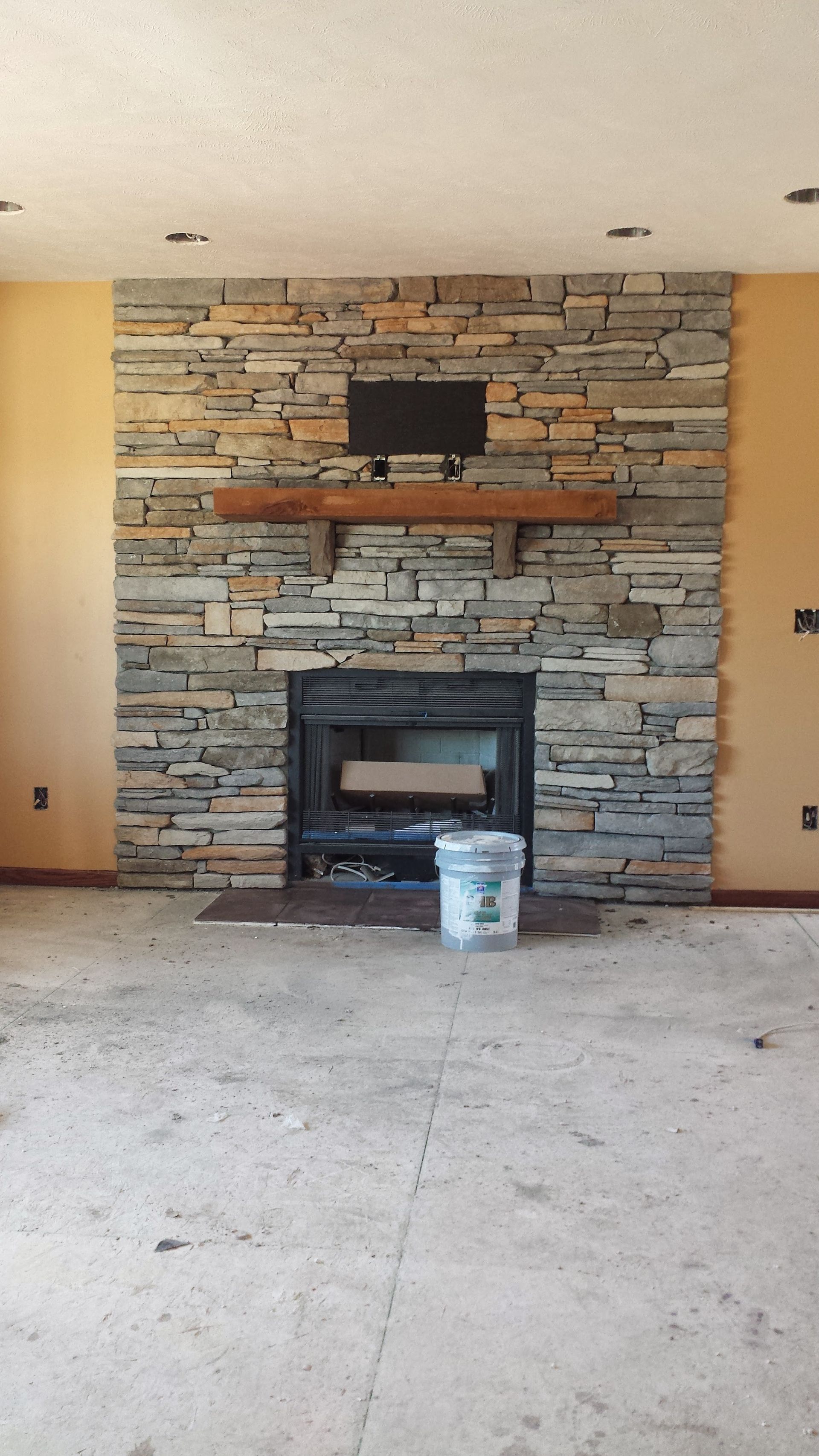 Stone fireplace wall with mounted TV shelf in a bare room, with a bucket on the floor.