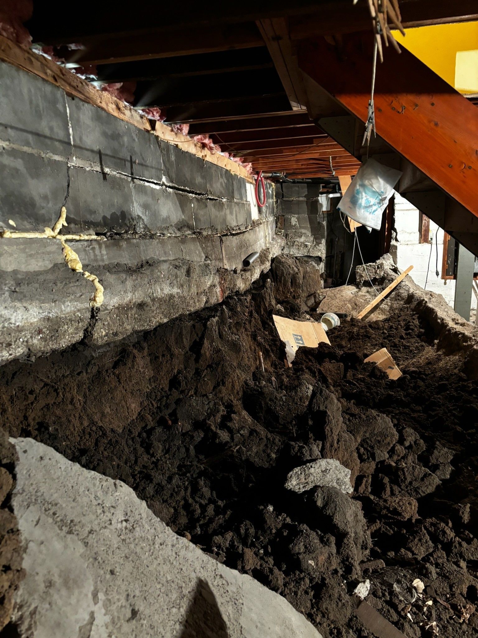 Collapsed basement floor with a large pile of dirt and cracked concrete walls under a house